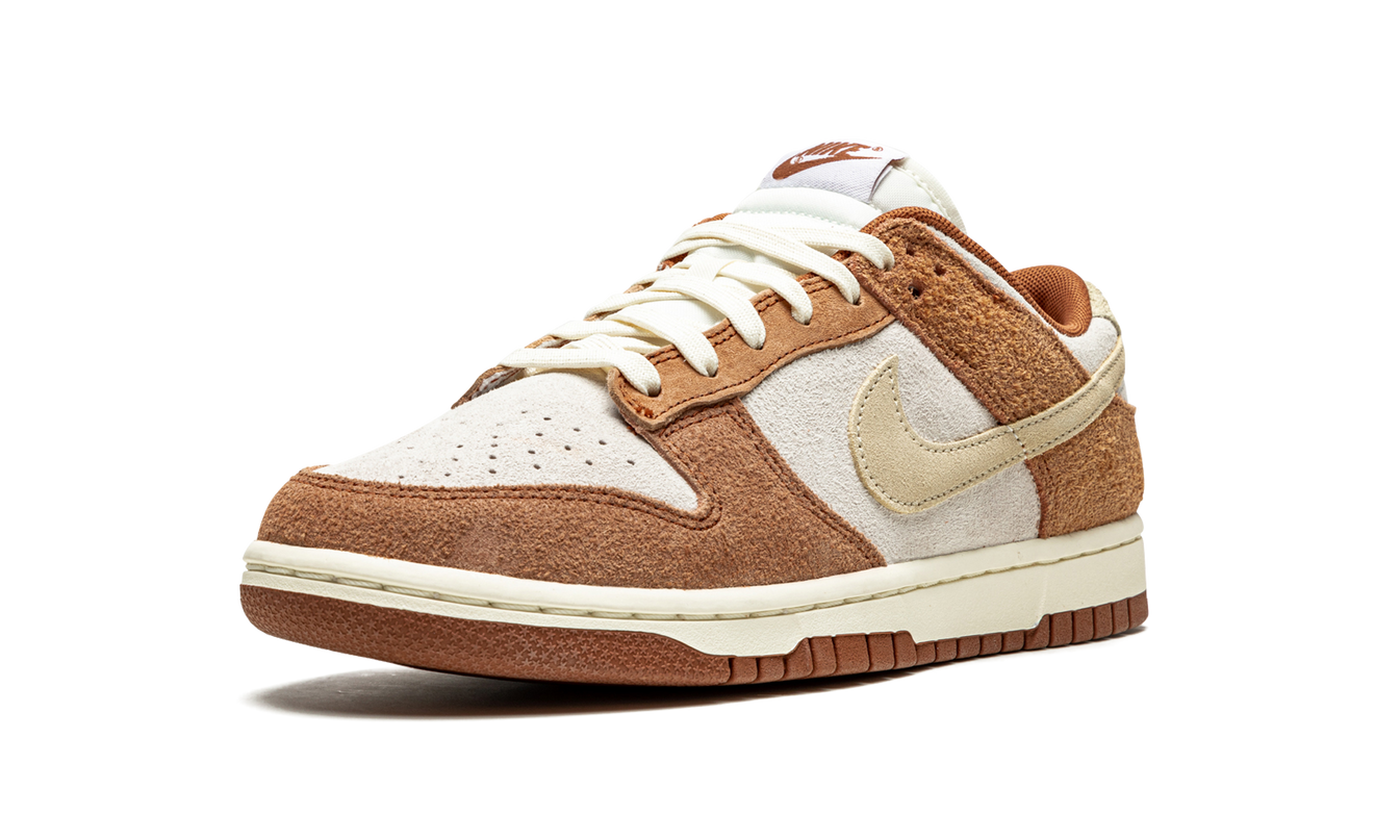 Nike Dunk Low PRM "Medium Curry" schoenen in geel en bruin leer, getoond op een witte achtergrond.