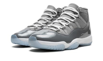 Zwarte en grijze Air Jordan 11 Retro schoenen met glanzende afwerking en witte details, gedragen door een persoon.