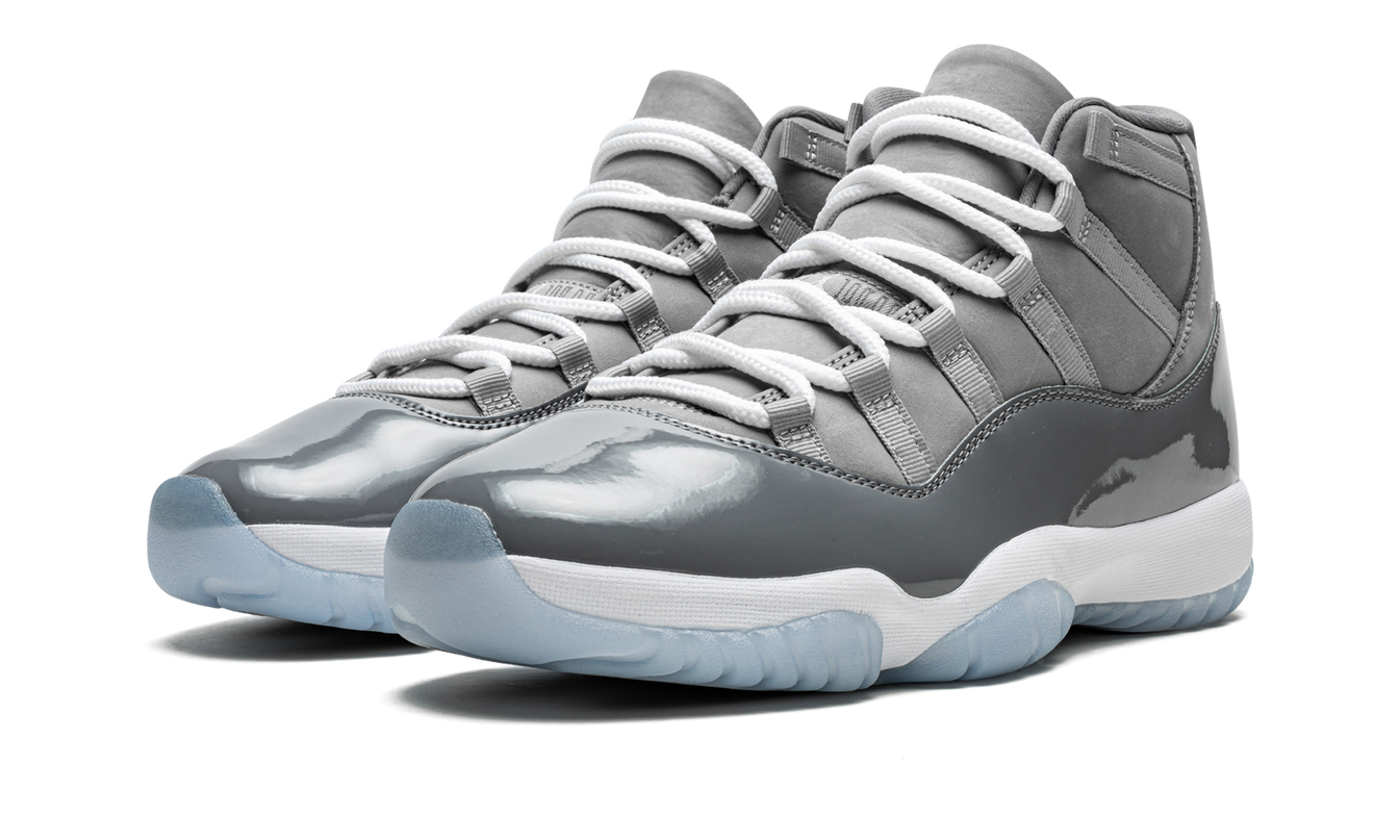Zwarte en grijze Air Jordan 11 Retro schoenen met glanzende afwerking en witte details, gedragen door een persoon.