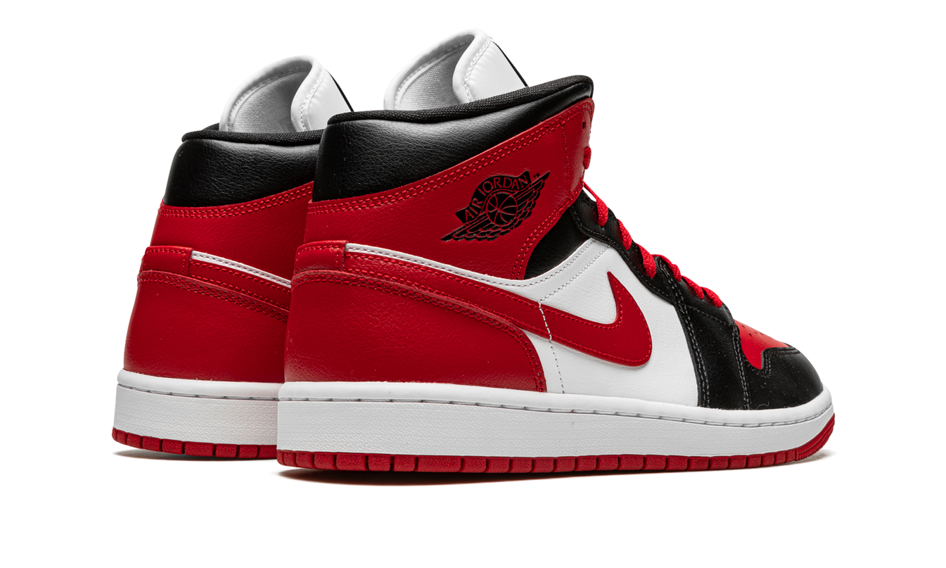 Zwarte en rode Air Jordan 1 MID WMNS schoenen met witte accenten en logo, zichtbaar in close-up op een witte achtergrond.