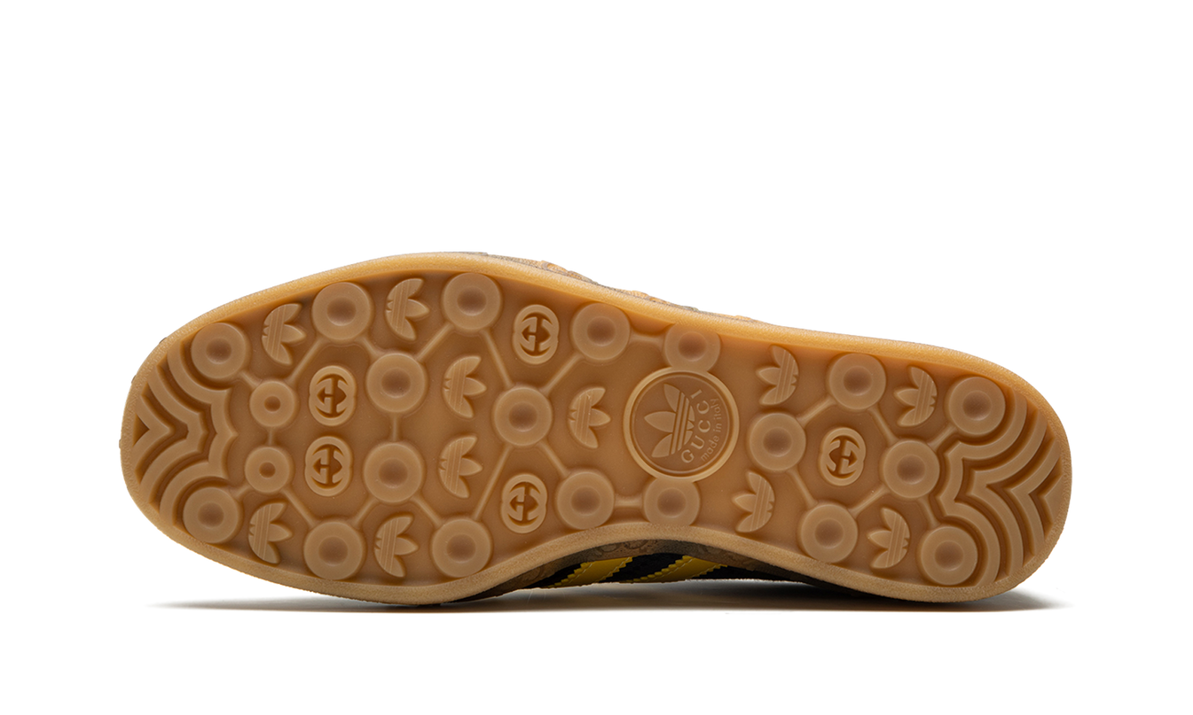 Zwarte Adidas Gucci Gazelle schoenen met GG Monogram patroon, zichtbaar van de zijkant op een witte achtergrond