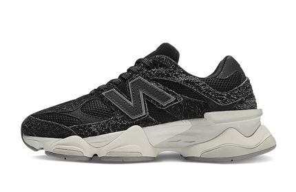 Zwarte New Balance 9060 schoenen met suède bovenkant en witte zool, gelegen op een houten vloer.