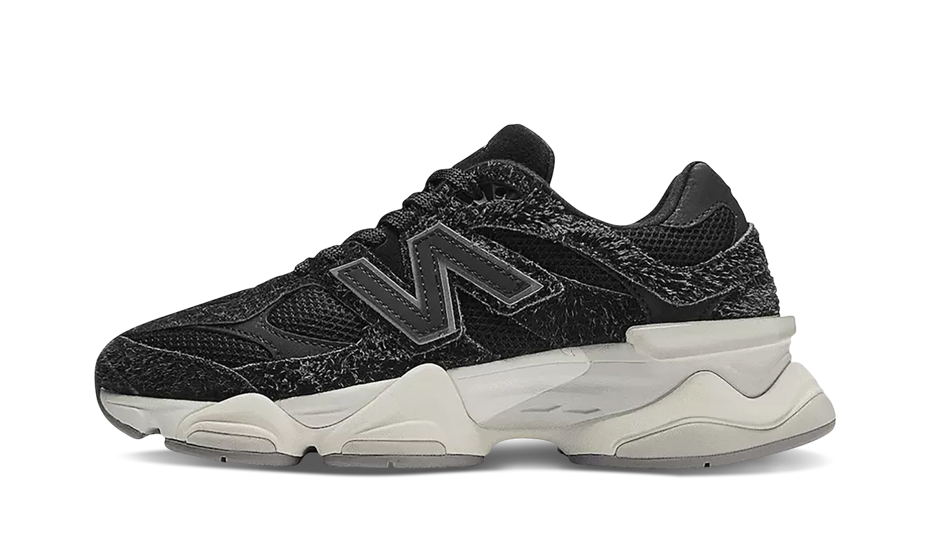 Zwarte New Balance 9060 schoenen met suède bovenkant en witte zool, gelegen op een houten vloer.