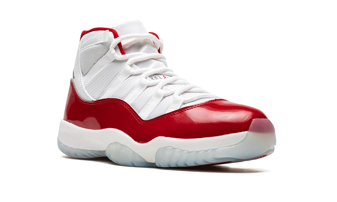 Zwarte en rode Air Jordan 11 "Cherry 2022" sneakers met glanzende afwerking en witte zool, gedragen door een model.