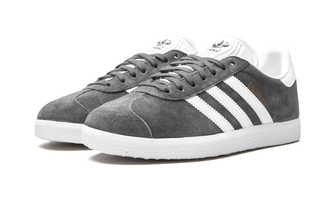 Donkere grijze Adidas Gazelle schoenen met zijstiksels en witte zool op een witte achtergrond.