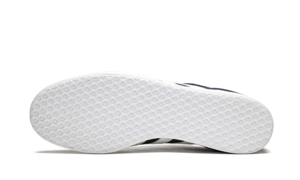 Donkerblauwe Adidas Gazelle schoenen met witte zool en gewatteerde details, gelegen op een houten vloer