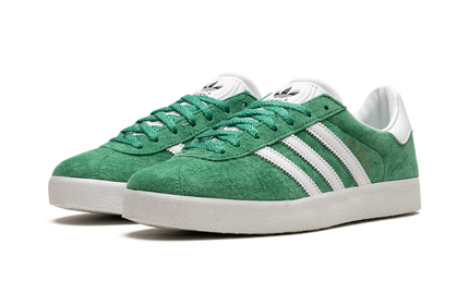 Donkergroene Adidas Gazelle 85 schoenen met witte veters en zool, close-up van de sportieve sneakers op een witte achtergrond.