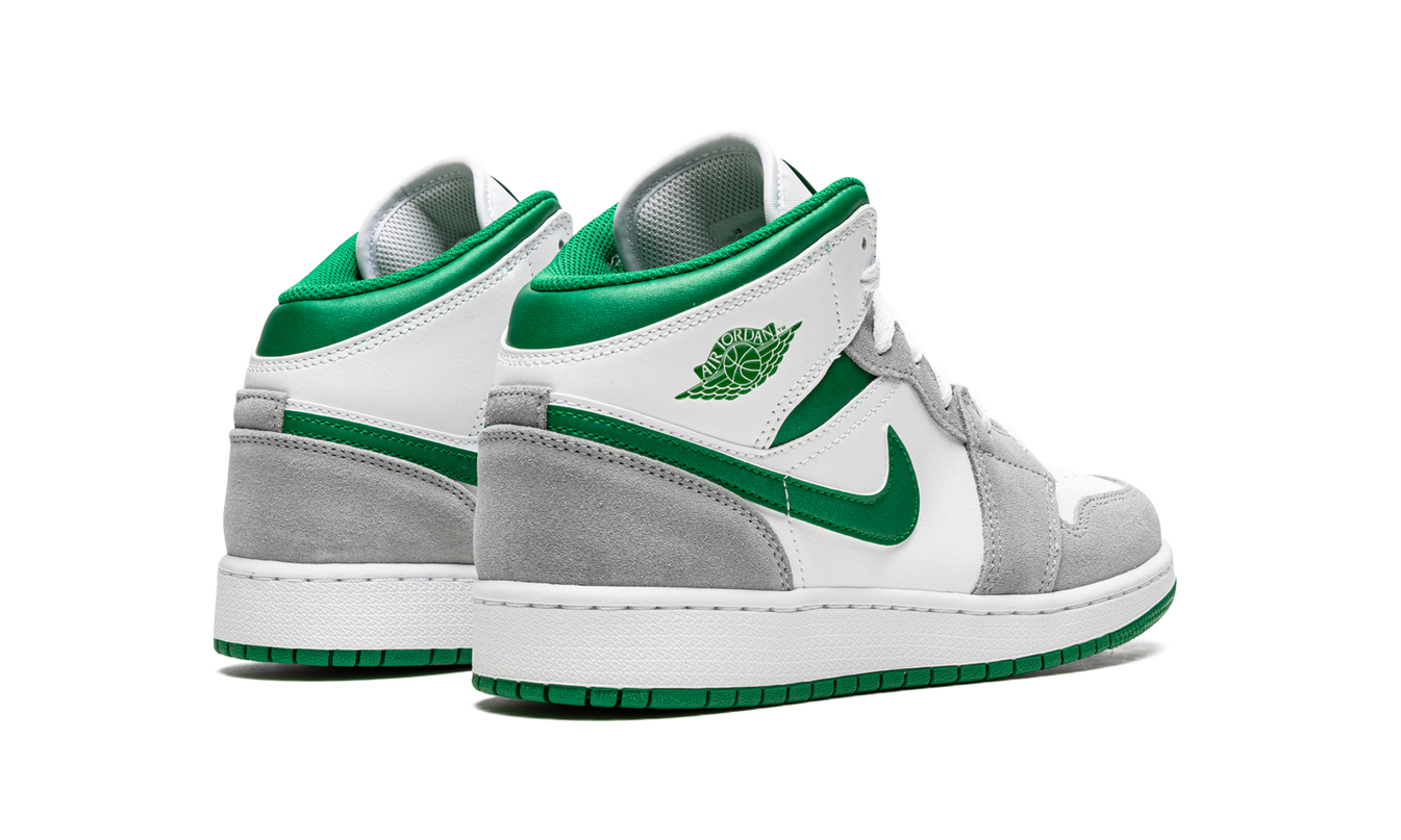 Witte en groene Air Jordan 1 Mid SE GS sneakers met grijze details en zwarte zolen, zichtbaar van de zijkant.